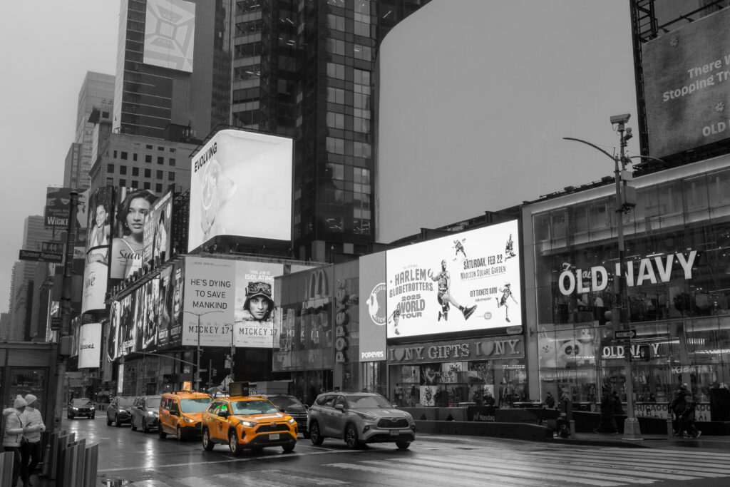 A black and white photo of times square, the only colour being two yellow taxis.